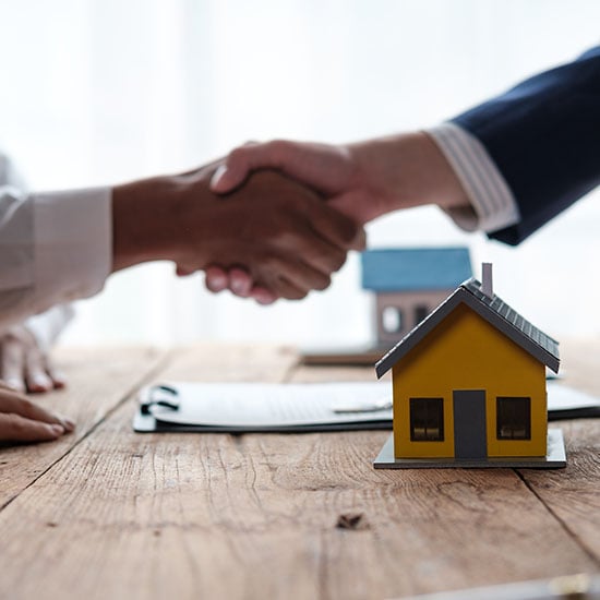Real Estate agent and client shaking hands above miniature model homes